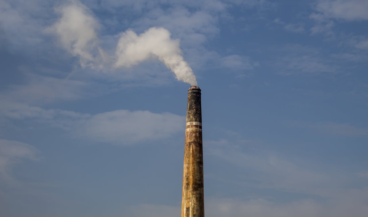 A factory chimney releasing smoke against a clear blue sky, highlighting air pollution.